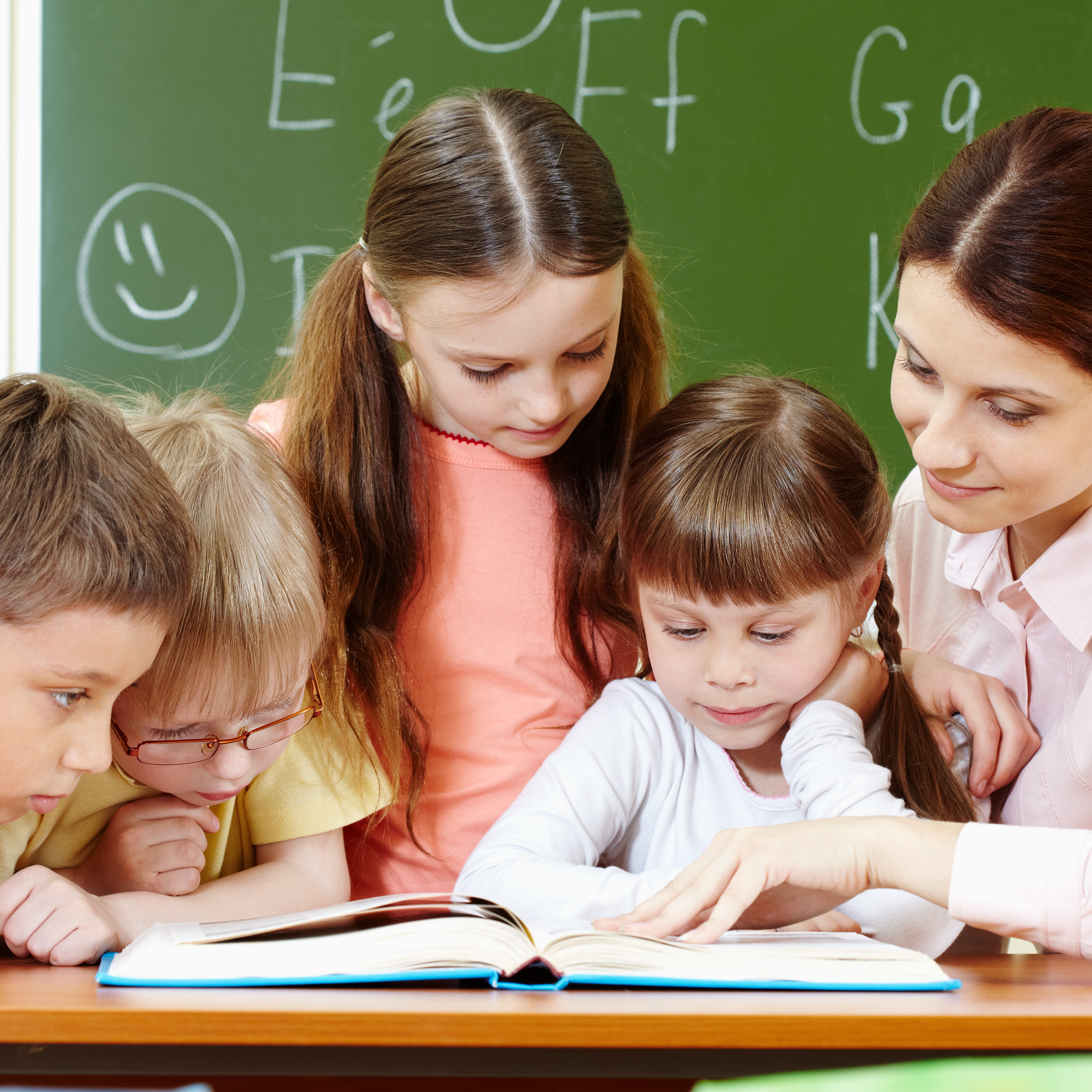 Portrait of smart schoolchildren and their teacher reading book in classroom