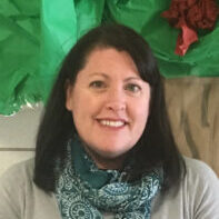 dark haired woman with blue scarf standing in front of tissue paper tree. This is the program director